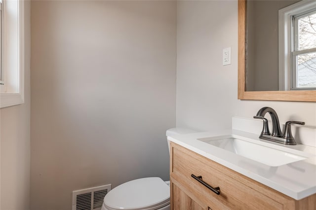 half bath with toilet, vanity, and visible vents