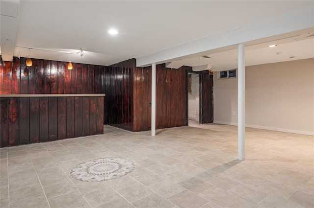 finished basement featuring wood walls, a bar, and baseboards