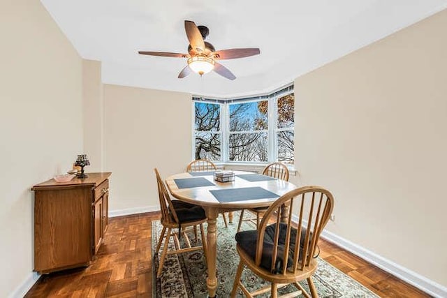 dining space with ceiling fan and dark parquet flooring