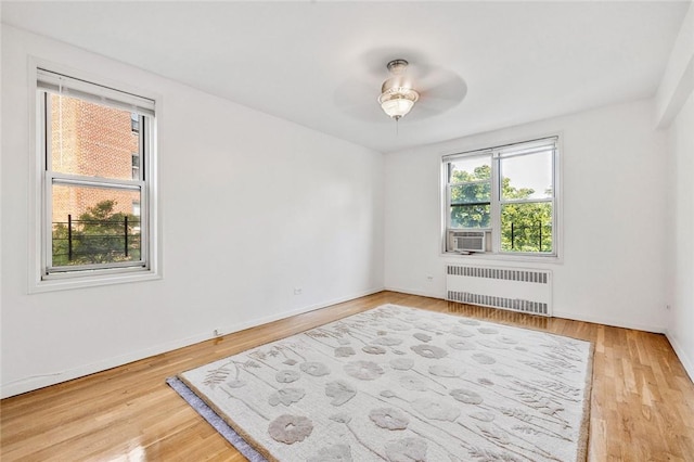 spare room featuring radiator, ceiling fan, cooling unit, and light wood-type flooring