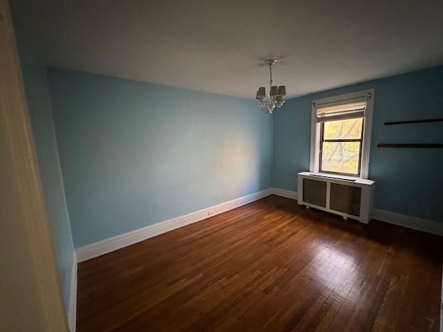 spare room with radiator, a chandelier, and dark wood-type flooring