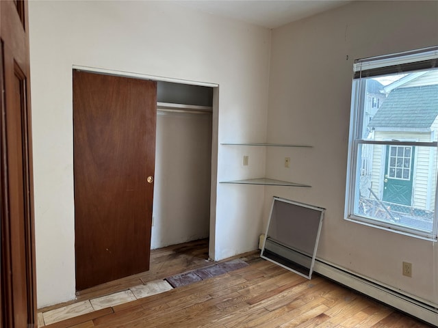 unfurnished bedroom with a baseboard radiator, light wood-type flooring, and a closet