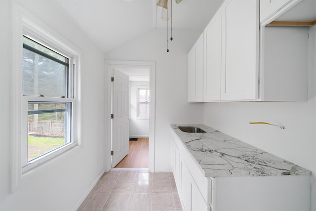 kitchen featuring white cabinets, light stone counters, lofted ceiling, and light hardwood / wood-style flooring