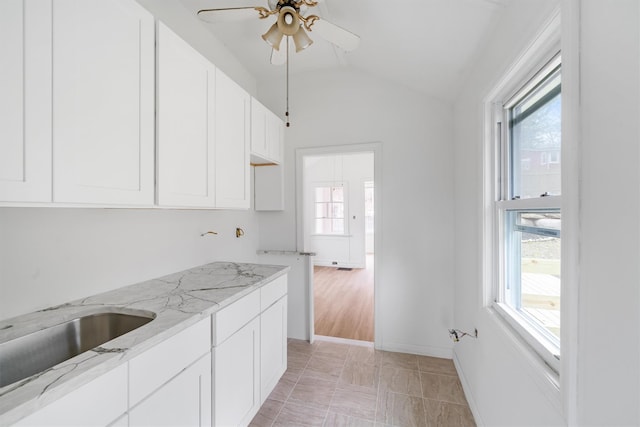 kitchen with light stone counters, white cabinetry, a wealth of natural light, and vaulted ceiling