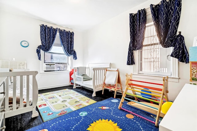 bedroom with a nursery area, cooling unit, dark hardwood / wood-style flooring, and multiple windows