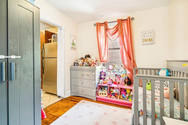 bedroom with a crib, stainless steel fridge, and light hardwood / wood-style flooring