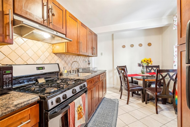 kitchen with sink, dark stone counters, decorative backsplash, light tile patterned flooring, and appliances with stainless steel finishes