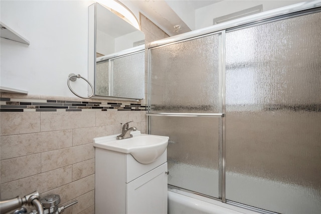 bathroom with combined bath / shower with glass door, vanity, and tile walls