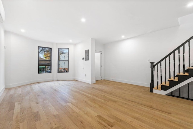 unfurnished living room featuring light hardwood / wood-style floors, a wall unit AC, and electric panel