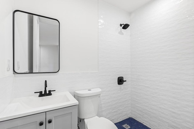 bathroom with a tile shower, vanity, toilet, and tile walls