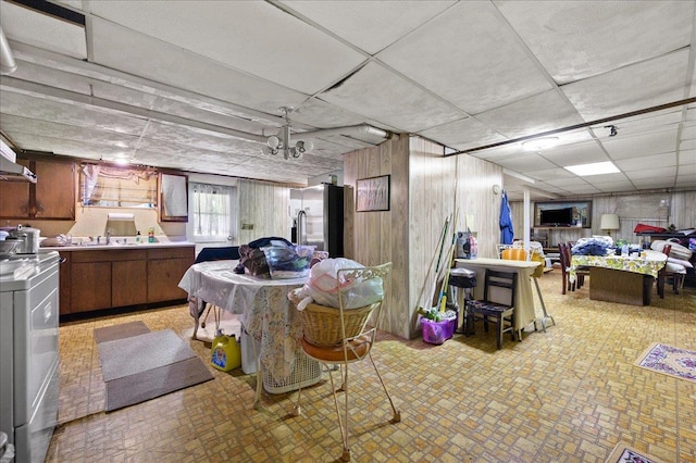 basement featuring wooden walls, sink, a drop ceiling, and stainless steel refrigerator with ice dispenser