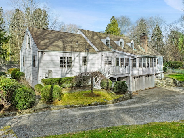 exterior space featuring driveway, a garage, a chimney, stairs, and a deck