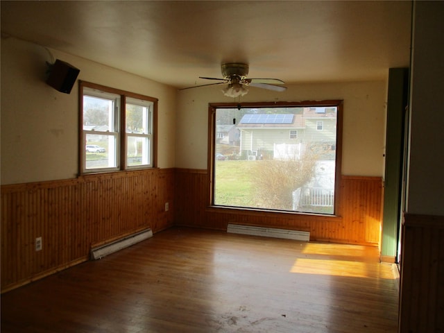 unfurnished room with hardwood / wood-style flooring, wooden walls, ceiling fan, and a baseboard heating unit