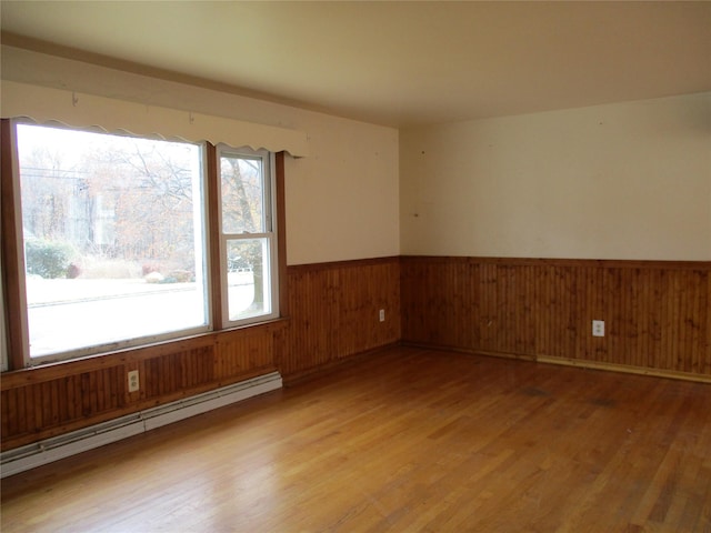 spare room featuring wooden walls, light wood-type flooring, and a baseboard heating unit