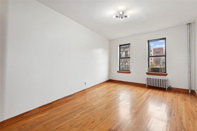 empty room with radiator heating unit, an inviting chandelier, and light wood-type flooring