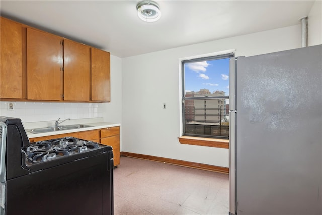 kitchen featuring decorative backsplash, gas stove, sink, and stainless steel refrigerator