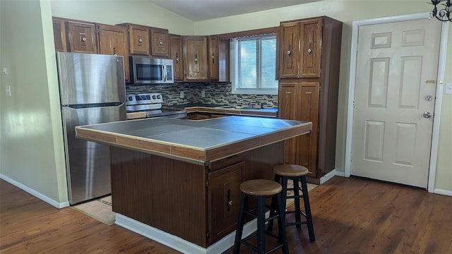 kitchen featuring a kitchen breakfast bar, vaulted ceiling, decorative backsplash, a kitchen island, and stainless steel appliances