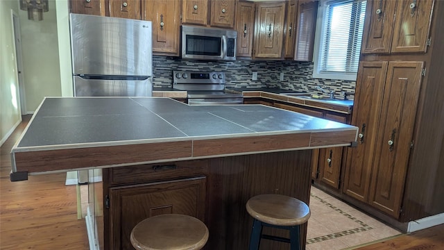 kitchen with a kitchen bar, decorative backsplash, stainless steel appliances, sink, and a center island