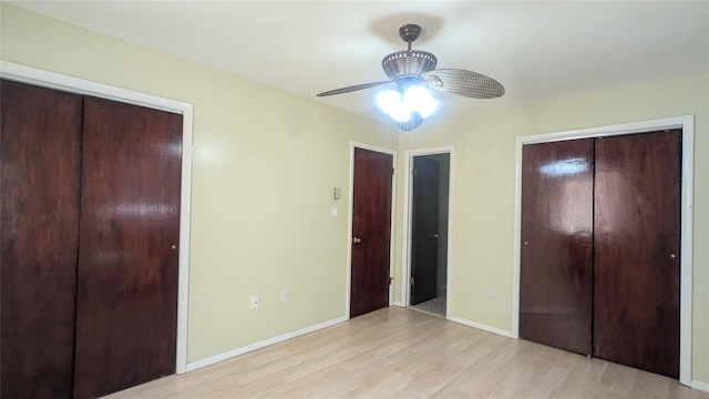 unfurnished bedroom with light wood-type flooring, ceiling fan, and multiple closets