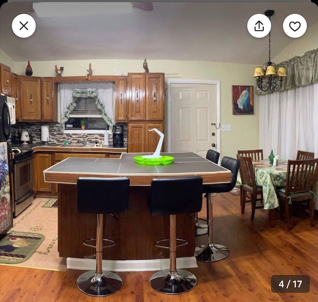 kitchen with decorative backsplash, stainless steel electric stove, pendant lighting, an inviting chandelier, and lofted ceiling