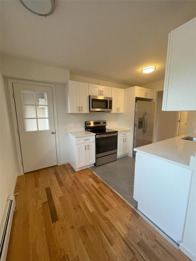 kitchen with appliances with stainless steel finishes, sink, a baseboard radiator, light hardwood / wood-style flooring, and white cabinetry