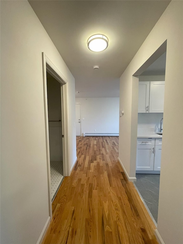 corridor with baseboard heating and light hardwood / wood-style floors