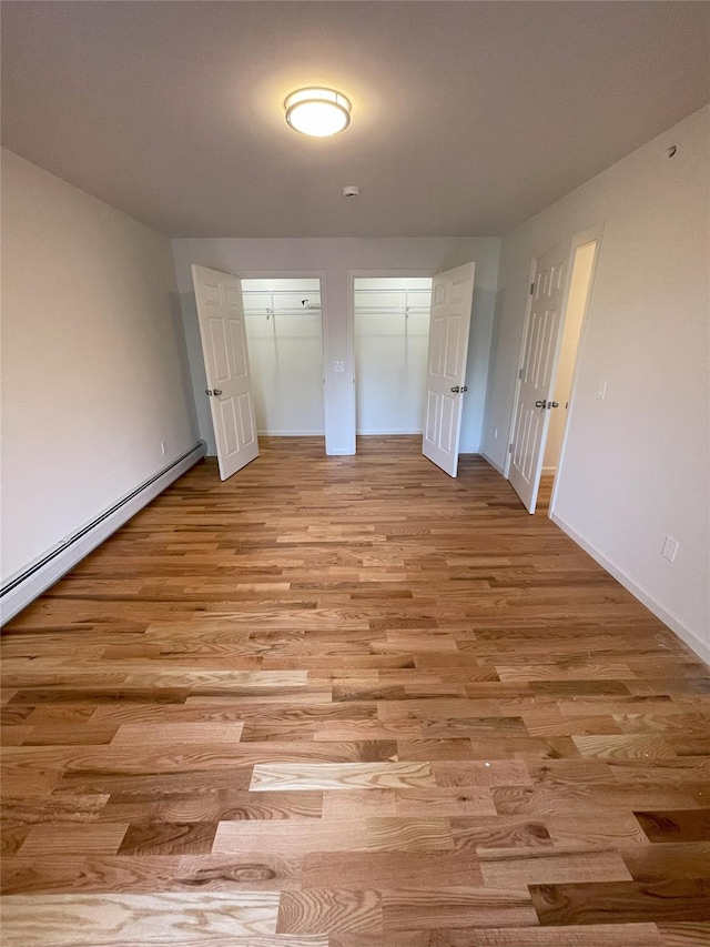 unfurnished bedroom with two closets, light hardwood / wood-style floors, and a baseboard radiator