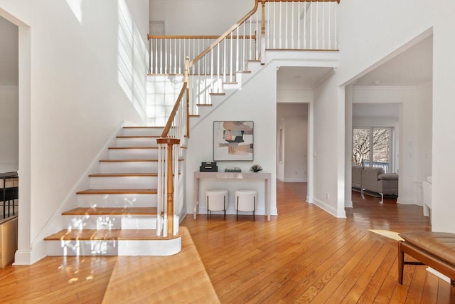 staircase featuring a high ceiling, ornamental molding, and wood-type flooring