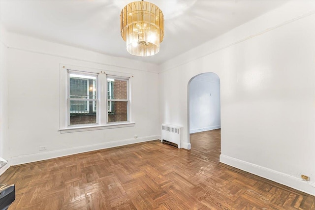 spare room featuring radiator, parquet flooring, and a chandelier