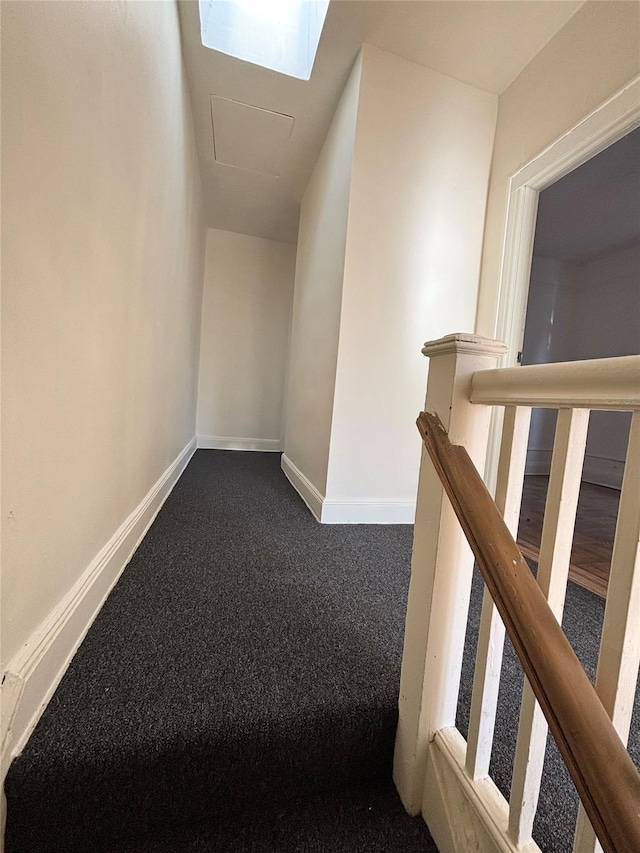 hall with dark colored carpet and a skylight