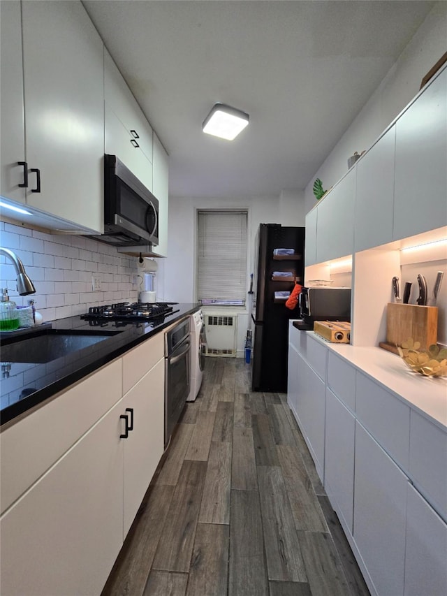 kitchen with radiator heating unit, white cabinetry, dark hardwood / wood-style flooring, and appliances with stainless steel finishes