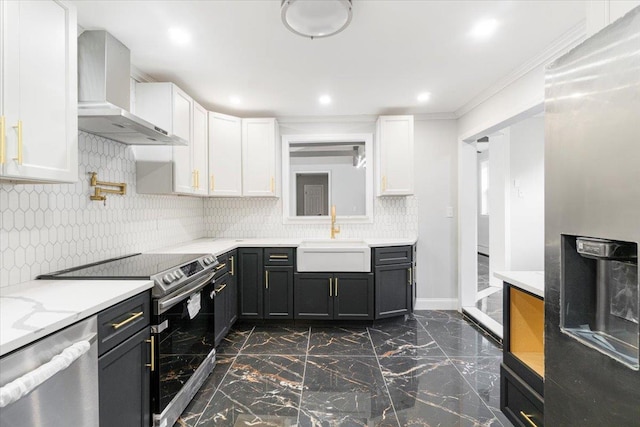 kitchen featuring appliances with stainless steel finishes, ornamental molding, sink, wall chimney range hood, and white cabinets