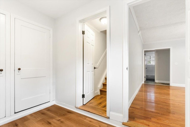 hall featuring a textured ceiling, hardwood / wood-style flooring, vaulted ceiling, and ornamental molding