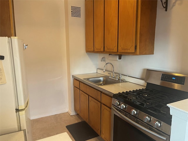 kitchen featuring light tile patterned floors, stainless steel gas stove, white refrigerator, and sink