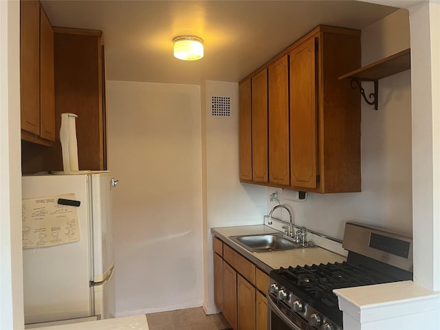 kitchen featuring stainless steel range with gas cooktop, sink, light tile patterned floors, and white refrigerator