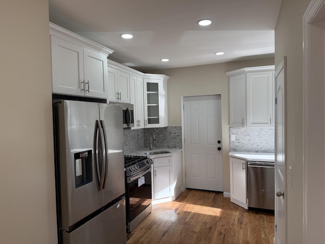 kitchen with tasteful backsplash, stainless steel appliances, sink, light hardwood / wood-style floors, and white cabinetry