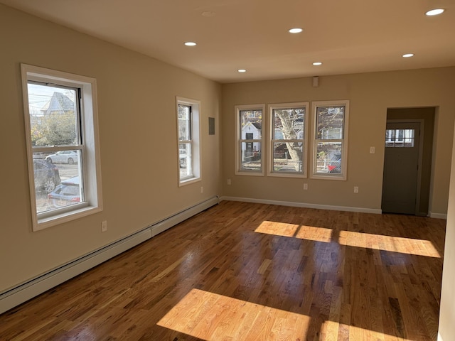 empty room featuring wood-type flooring and a baseboard heating unit