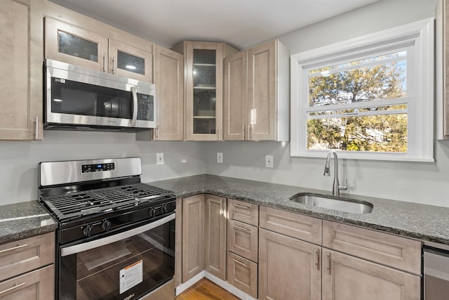 kitchen featuring dark stone counters, sink, light wood-type flooring, light brown cabinetry, and appliances with stainless steel finishes