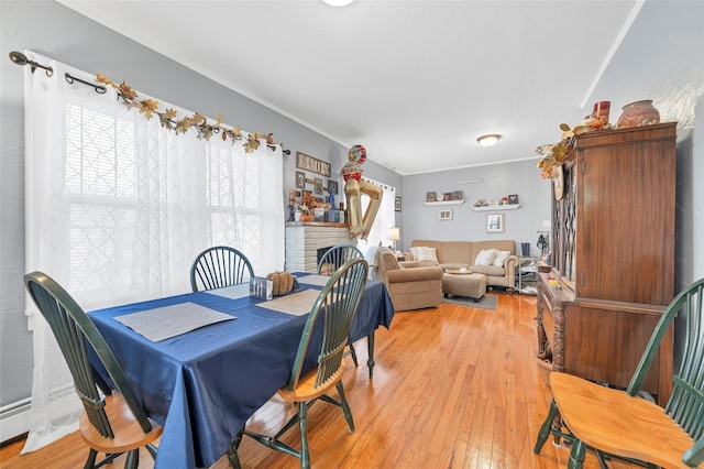 dining area with hardwood / wood-style floors, ornamental molding, and a brick fireplace