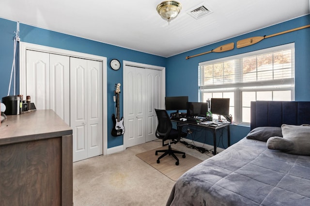 bedroom with two closets, visible vents, carpet floors, and multiple windows