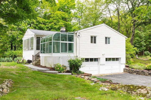 rear view of house featuring a sunroom, a garage, and a yard