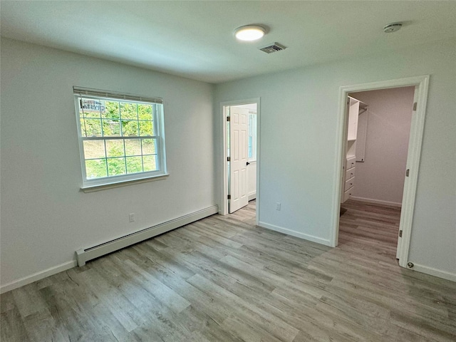 unfurnished bedroom featuring light wood-type flooring, connected bathroom, and a baseboard heating unit