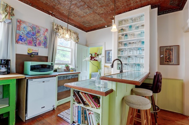 kitchen featuring white appliances, dark wood-type flooring, decorative light fixtures, tile counters, and a breakfast bar area