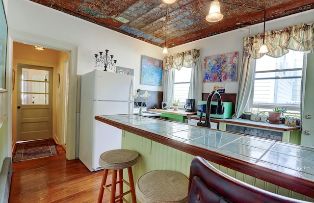 kitchen with hardwood / wood-style floors, pendant lighting, tile countertops, a kitchen breakfast bar, and white fridge