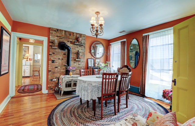 dining room with a notable chandelier, a wood stove, light hardwood / wood-style flooring, and a wealth of natural light