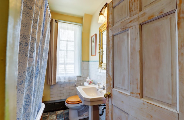 bathroom with plenty of natural light, toilet, sink, and tile walls