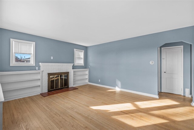 unfurnished living room featuring a brick fireplace, a wealth of natural light, and hardwood / wood-style flooring