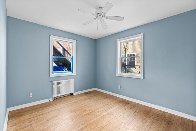 unfurnished room featuring radiator, a wealth of natural light, ceiling fan, and light wood-type flooring