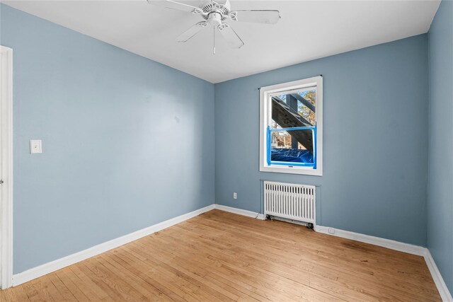 spare room featuring radiator, ceiling fan, and light wood-type flooring