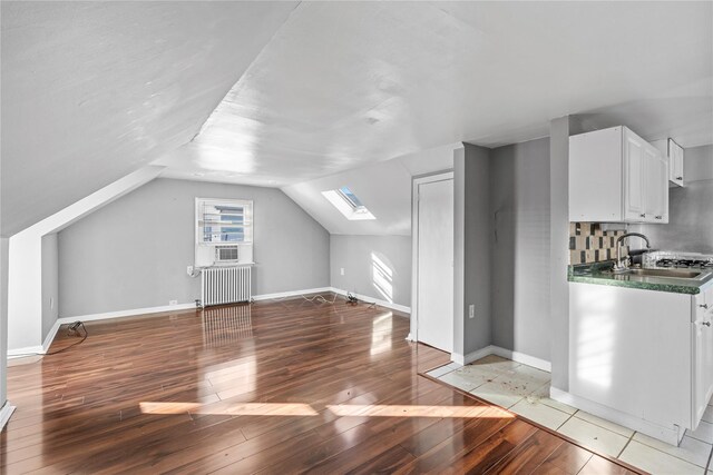 additional living space featuring vaulted ceiling with skylight, sink, radiator, and light hardwood / wood-style flooring